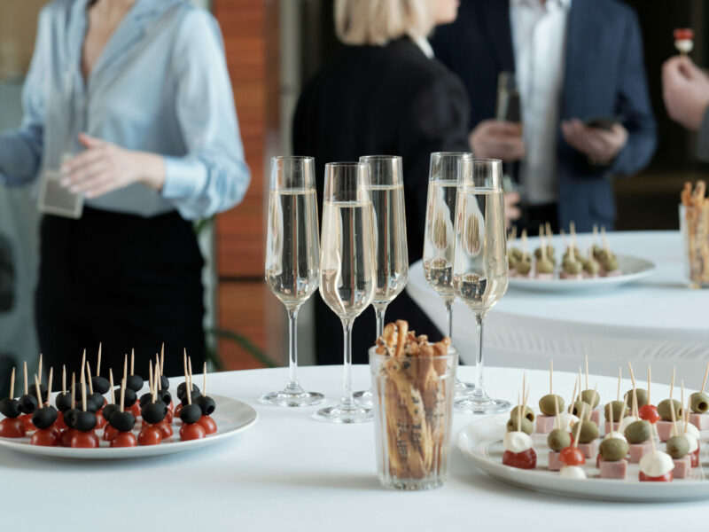 Two plates with appetizing canape and group of champagne in flutes standing on served tables prepared for celebration